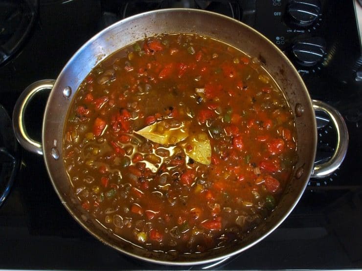 Sauce simmering with bay leaves on stovetop.