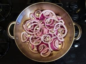 Raw purple onion circles in pan on stovetop.