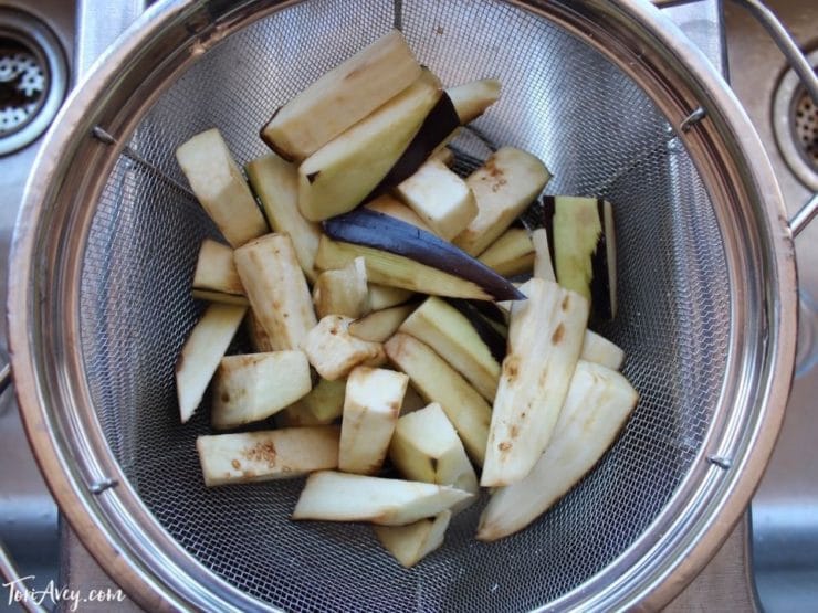 Eggplant pieces in colander over sink.