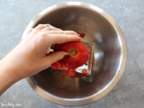 Hand grating tomato over bowl.