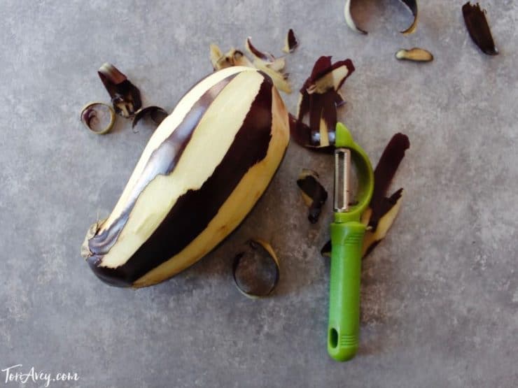 Eggplant half peeled in strips with peeler.