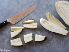 Eggplant cut into chunks with chef's knife on concrete background.