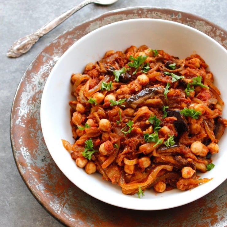 Mnazaleh - Recipe with Chickpeas, Eggplant and Onions in white bowl on metal platter with spoon.