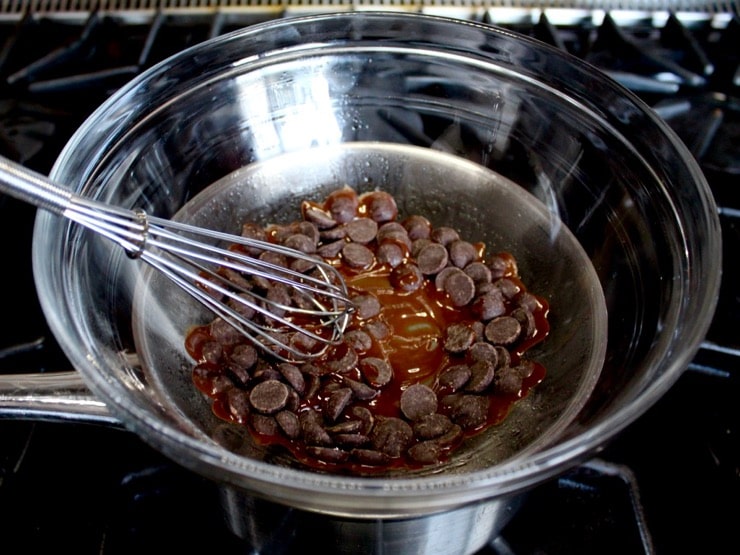 Chocolate pieces melting in double boiler with whisk on stovetop.
