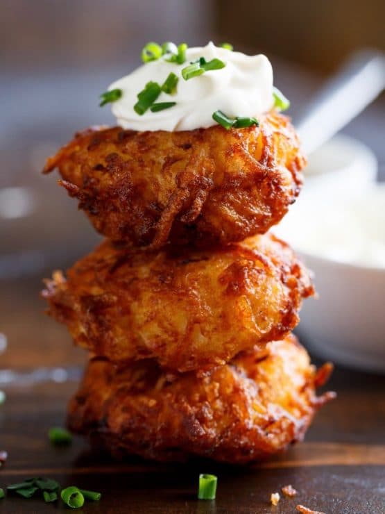 Pile of three latkes on a white plate with sour cream and chives.