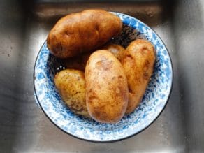 5 large Russet potatoes in blue speckled colander over sink.