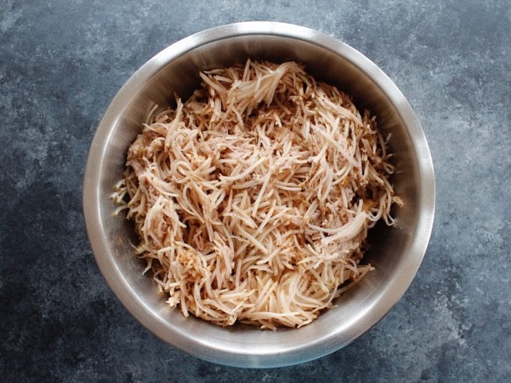 Potato shreds in large mixing bowl on concrete background.