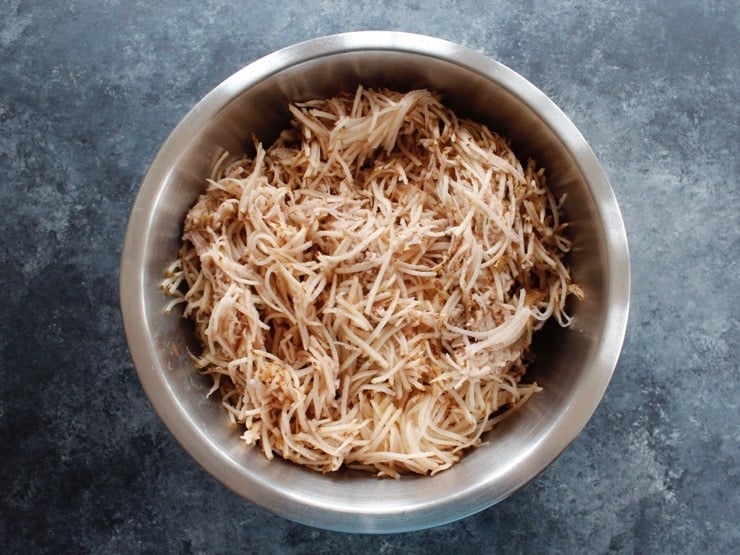 Potato shreds in large mixing bowl on concrete background.