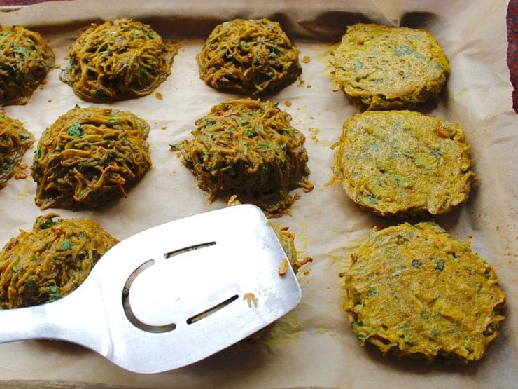 Flipping and flattening potato pancakes with a stainless steel spatula that's on a baking sheet and tray