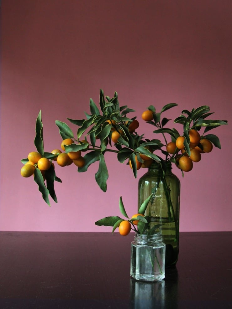 Wide shot of kumquat branches in green vintage glass bottle and clear jar.