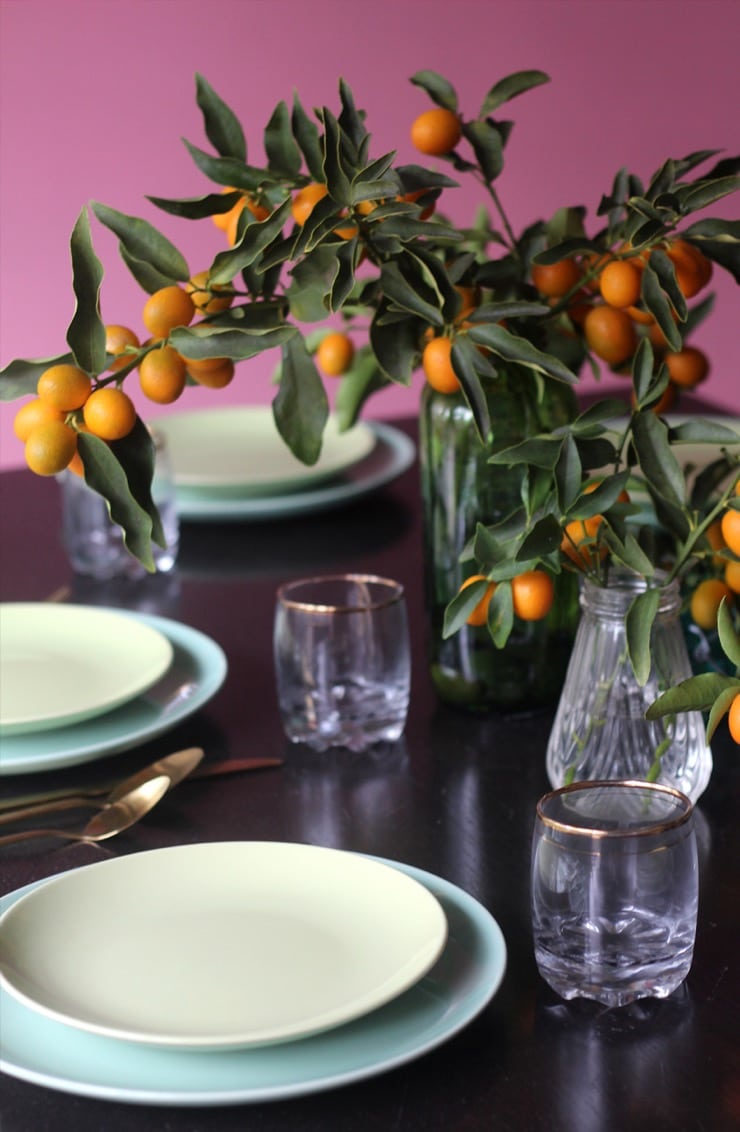 Table setting - plates, utensils and glass with gold accent. Clear vase with kumquat branch centerpiece.