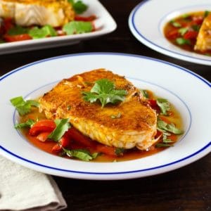 Moroccan paprika fish on a bed of vegetables topped wth fresh green herbs in a white bowl.