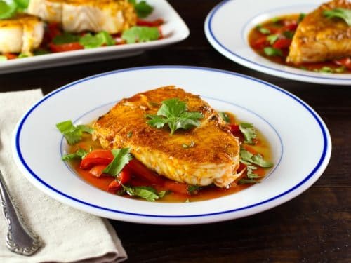 Moroccan paprika fish on a bed of vegetables topped wth fresh green herbs in a white bowl.