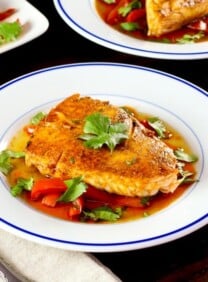 Moroccan paprika fish on a bed of vegetables topped wth fresh green herbs in a white bowl.
