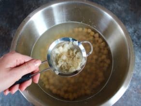 A person holds a drainer over a bowl of food containing chickpeas