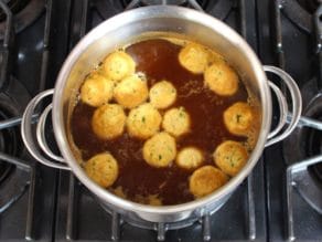 Matzo balls cooking in a large pot of broth.