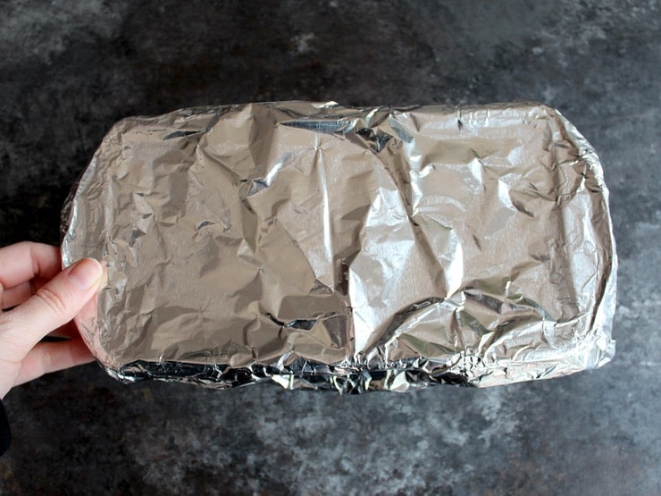 Small loaf pan covered with parchment and foil on grey countertop.