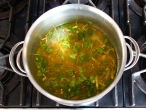 A large stock pot filled with soup stock and herbs.