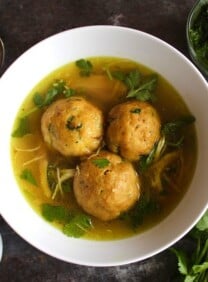 Yemenite matzo ball soup with three large matzo balls in a white bowl with a spoon on the side