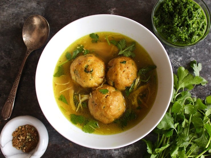 Yemenite matzo ball soup with three large matzo balls in a white bowl with a spoon on the side
