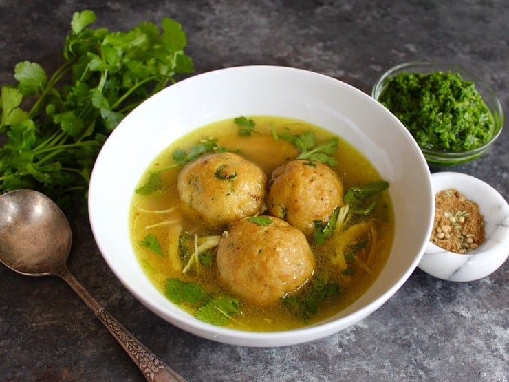 Yemenite matzo ball soup with three large matzo balls in a white bowl on a silver tray.