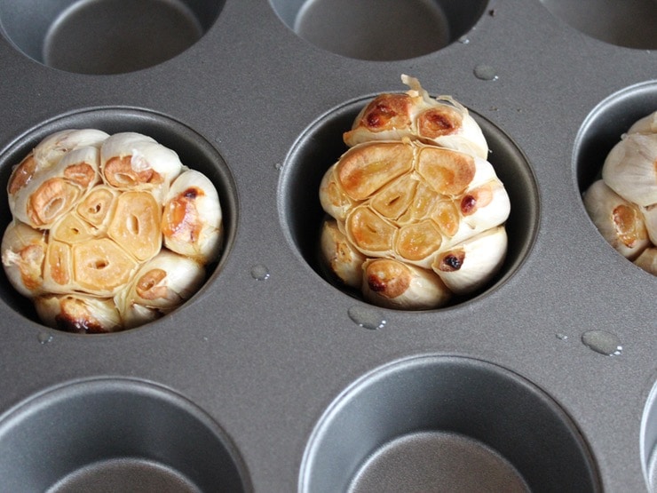 Three heads of roasted garlic with exposed cloves in muffin pan.