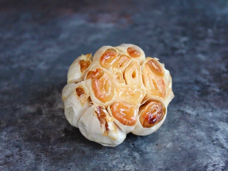 Head of roasted garlic with exposed cloves on grey countertop.