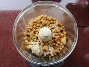 Hummus ingredients combined in food processor ready to blend - chickpeas, tahini, roasted garlic, spices, salt.