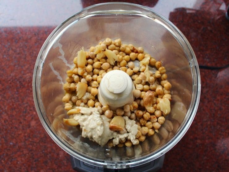 Hummus ingredients combined in food processor ready to blend - chickpeas, tahini, roasted garlic, spices, salt.