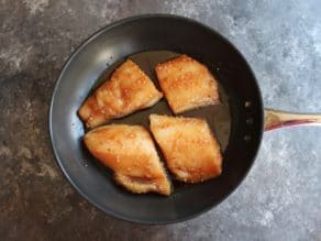 Four marinated Teriyaki Black Cod fillets, uncooked, in a skillet with olive oil on countertop.