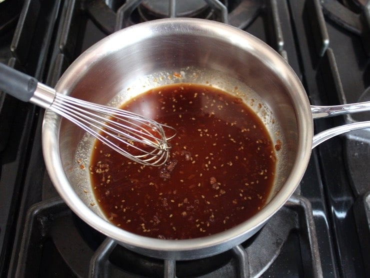 Whisking thickened teriyaki sauce in pan on stovetop.