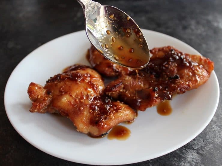Spooning sauce over Spicy Teriyaki Broiled Chicken Thighs on white plate.