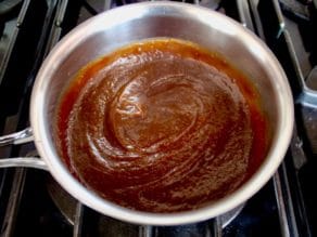 Thick glossy brown sauce in stainless steel saucepan on stovetop.