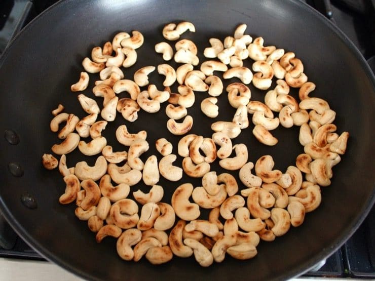 Cashews toasting in black nonstick skillet, browned.