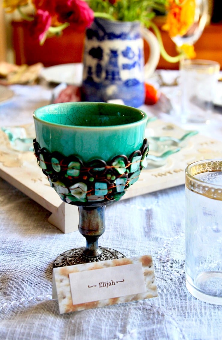 A turquoise Elijah cup sitting on a table decorated for the Passover seder.