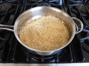 Raw rinsed quinoa in stainless skillet on stovetop.