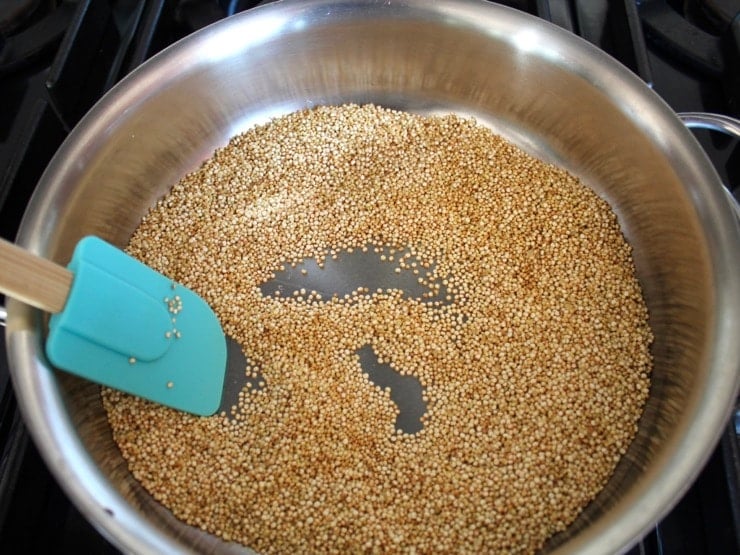 Quinoa toasting in stainless steel skillet on stovetop, stirred with spatula.
