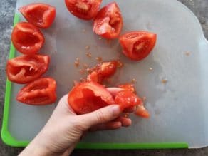 Fingers seeding tomato slices on cutting board.