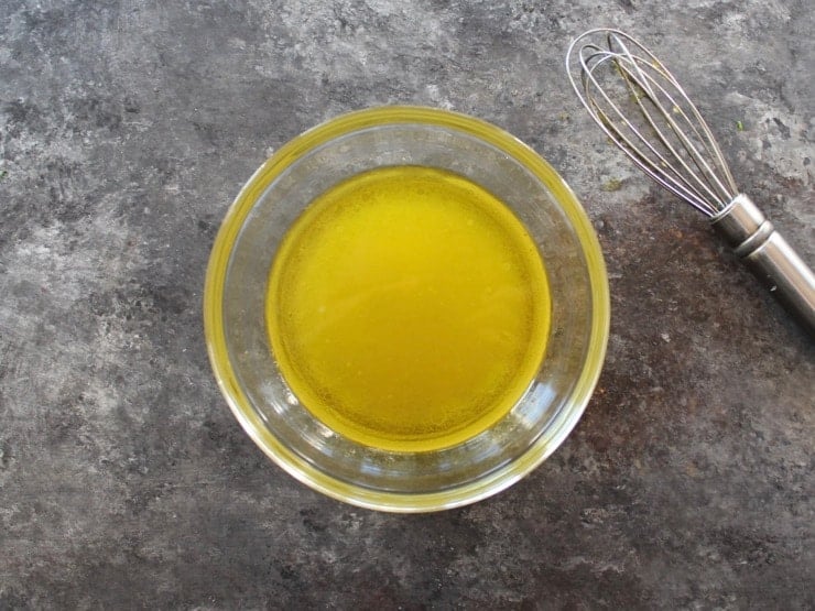 Overhead shot of olive oil dressing in glass bowl with whisk.