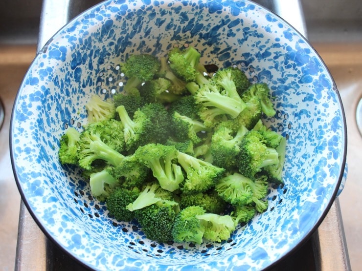 Steamed broccoli in blue speckled colander in sink
