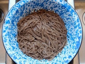 Cooked soba noodles in blue speckled colander in sink