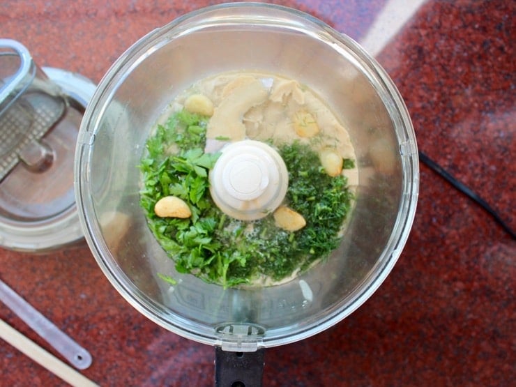 Overhead shot of food processor with ingredients for Herb Tahini Sauce inside.