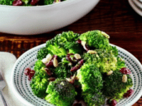 A bowl and plate of colorful broccoli craisin salad made with broccoli florets