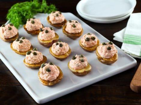Overhead view of a tray of small roasted potatoes topped with a lox topping and garnished with capers