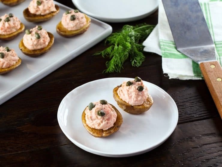 Small roasted potatoes topped with a lox topping and garnished with capers on a white plate.