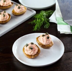 Small roasted potatoes topped with a lox topping and garnished with capers on a white plate.
