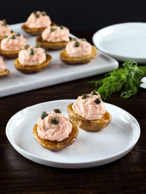 Small roasted potatoes topped with a lox topping and garnished with capers on a white plate.
