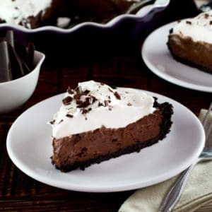 Slice of chocolate pie topped with whipped cream and chocolate shavings on a white plate.