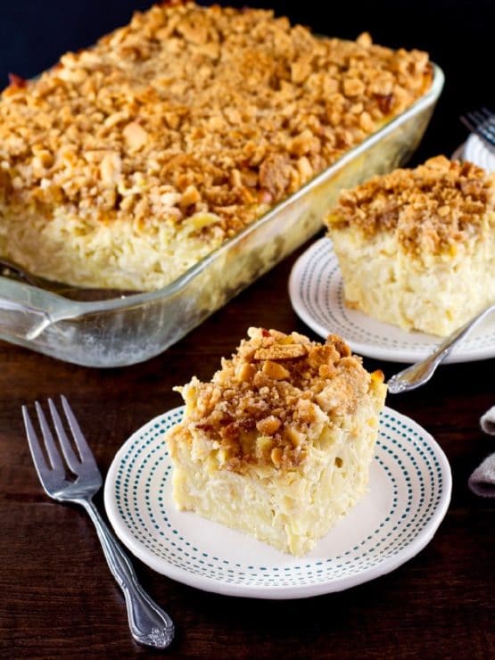 A square slice of kugel with a crunchy cookie topping on a white plate with a decorative border.