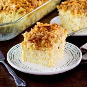 A square slice of kugel with a crunchy cookie topping on a white plate with a decorative border.